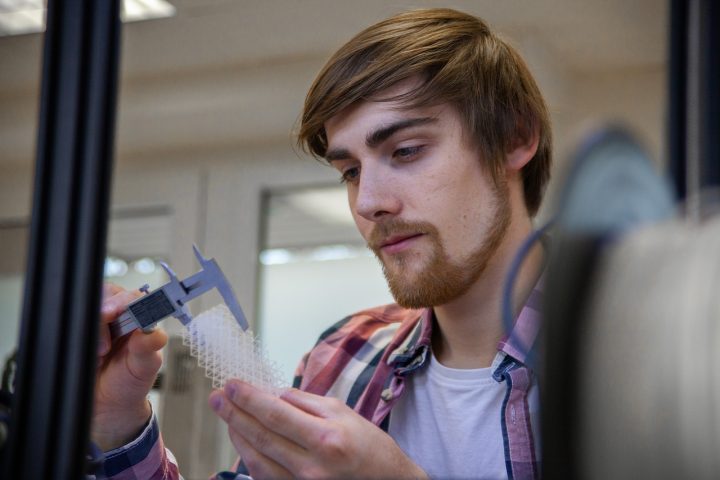 Mies mittaa työntömitalla 3D-tulostettua osaa.
